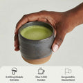 Mann hält eine handgemachte Keramiktasse mit Mushroom Matcha vor grauem Hintergrund.